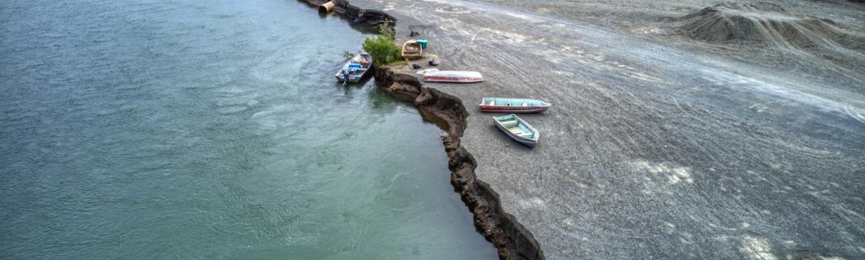 Aerial view of a gravel bar eroding into the river, with four boats at the erosion face.
