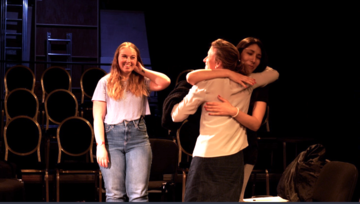 three actors on stage, two are hugging