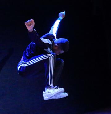 Man jumbing with arms outstretch on the side, wearing 3 stripped tracksuit